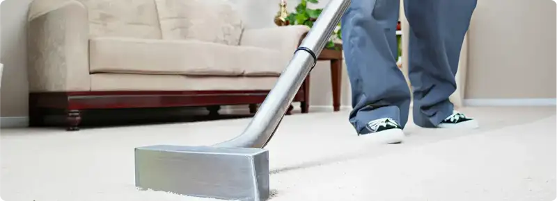 Carpet cleaning technician using a hot-water extraction wand on a light-colored carpet in a living room, Rockford, IL.