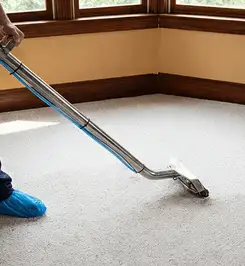 Steam carpet cleaning technician using a hot-water extraction wand on a residential carpet, wearing blue protective shoe covers Rockford, IL.