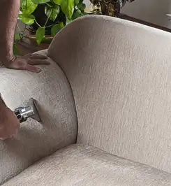 Professional upholstery cleaner deep-cleaning a fabric sofa with a handheld extraction tool and hose Rockford, IL.