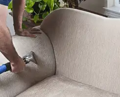 Professional upholstery cleaner deep-cleaning a fabric sofa with a handheld extraction tool and hose in Rockford, IL.